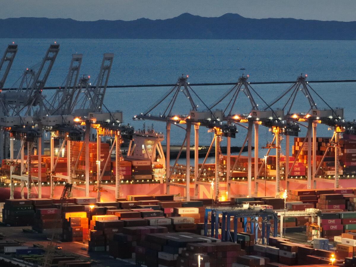 An aerial view of the Port of Long Beach at dusk with stacked containers and lighted structures.