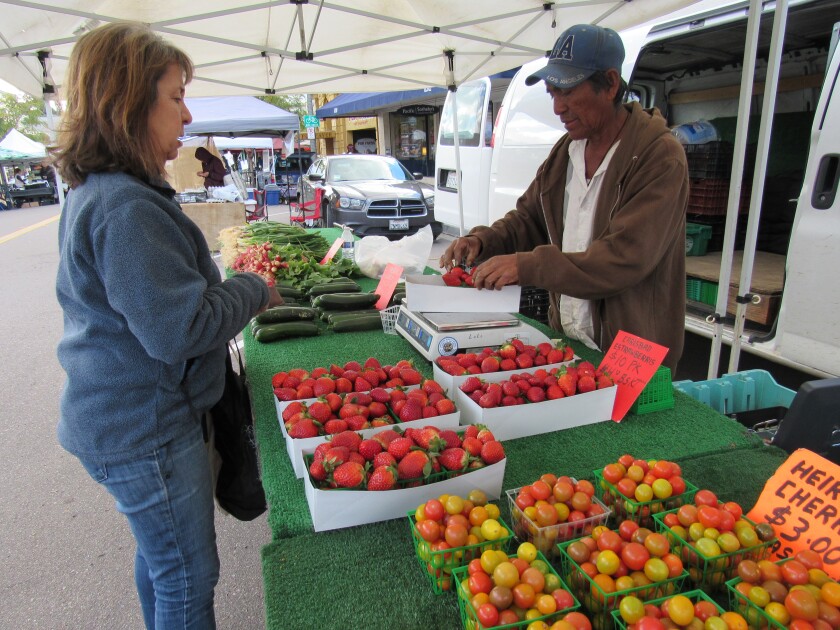 In this file photo from last fall, shopper Trish Watlington pays for fresh strawberries at The La Mesa Certified Farmers' Market. The popular market in the downtown Village area has been shut down to help stop the spread of the coronavirus but its managers, Brian Beevers and Vince Perez, have started an "on-the-go" market for pickup that includes many favorite items that were available on Fridays along La Mesa Boulevard.