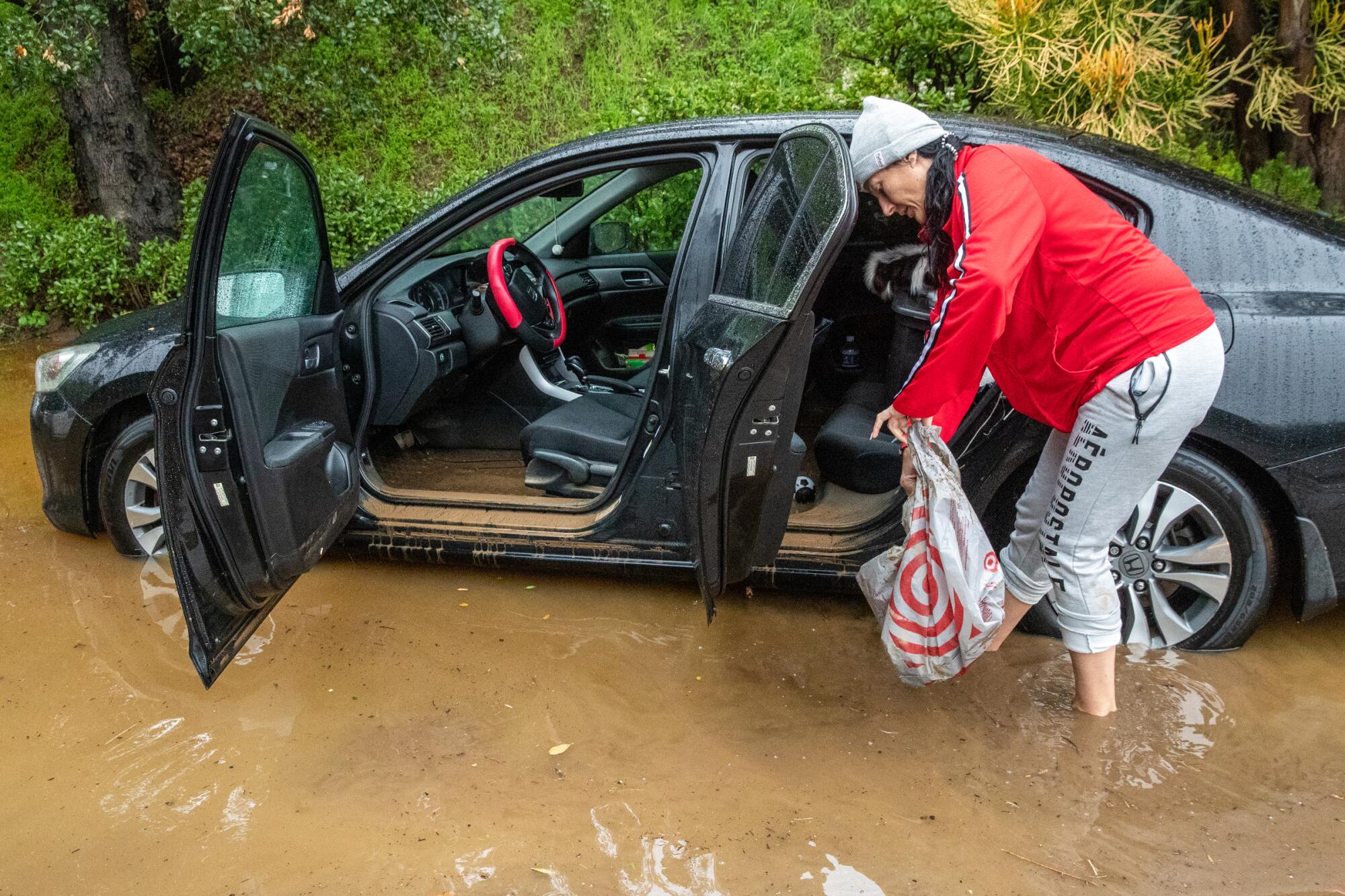 Gabriell Lambert cleans her car flooded by muddy water that came down hillside, caused by heavy rain