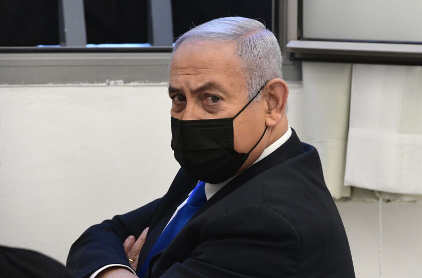 Benjamin Netanyahu, wearing a mask, sits with his arms crossed.