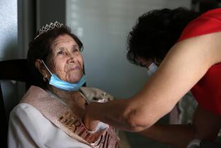 LOS ANGELES, CA - OCTOBER 03: Paula Cabrera places a flower pin on her mother, Angelita Arellano's coat for her 98th birthday party in East Los Angeles on Saturday, Oct. 3, 2020 in Los Angeles, CA. Angelita has 8 children, 36 great-grandchildren and family and friends came from near and far to celebrate. (Dania Maxwell / Los Angeles Times)