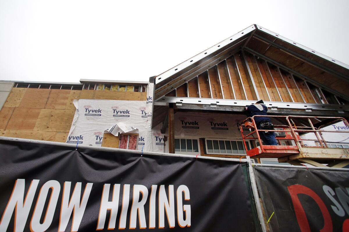 A "now hiring" sign hangs nearby as a builder works on a commercial property under construction in Peabody, Mass., on Jan. 12.