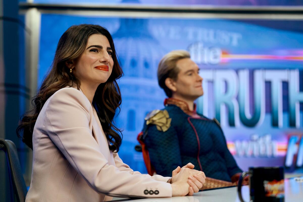 A woman in a suit and a man in a superhero outfit sit next to each other.