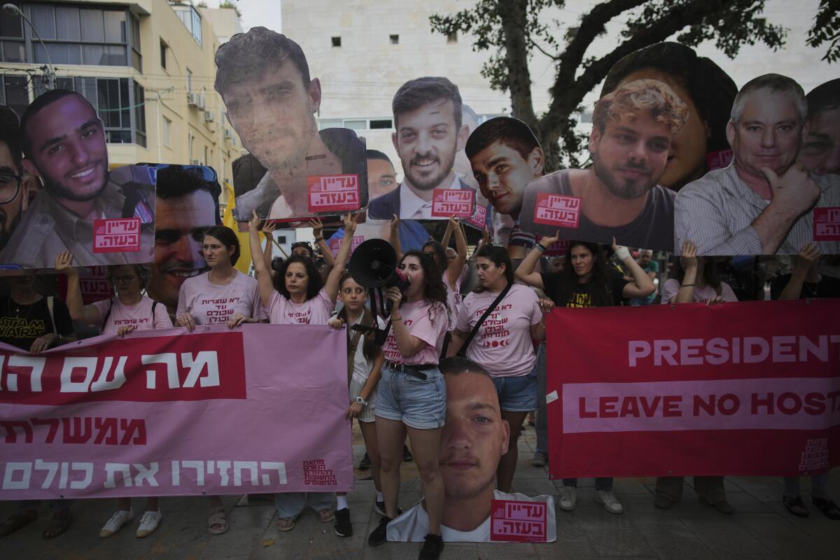 Cutout images of heads are carried above people in pink shirts protesting Israeli hostages held by Hamas in Gaza.