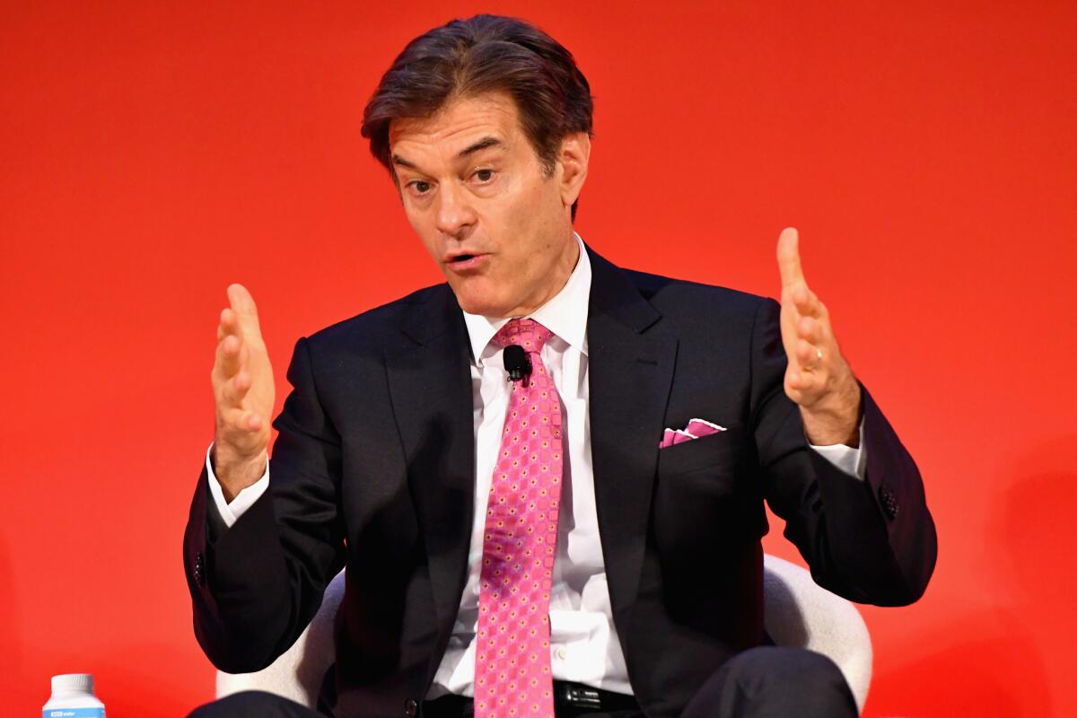 Dr. Mehmet Oz gestures with his hands while wearing a dark suit and pink tie.