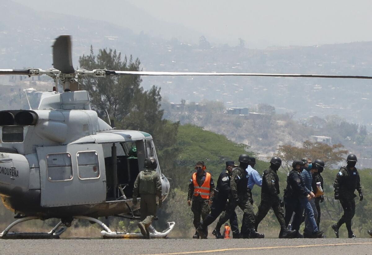 A line of people, some in police and military uniforms and helmets, walk away from a helicopter 