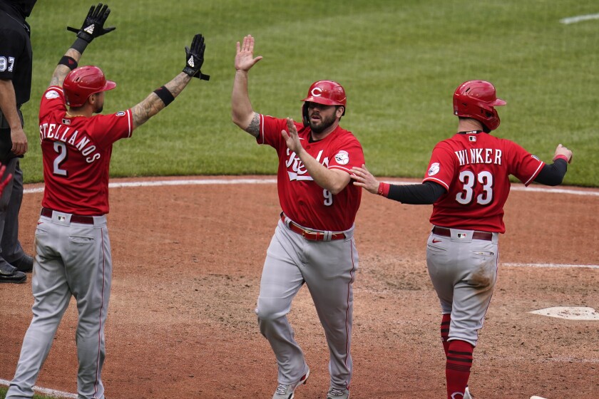 Cincinnati Reds' Mike Moustakas (9) is greeted by Nick Castellanos (2) and Jesse Winker after they all scored on a double by Eugenio Suarez off Pittsburgh Pirates relief pitcher Duane Underwood Jr. during the tenth inning of a baseball game in Pittsburgh, Wednesday, May 12, 2021.(AP Photo/Gene J. Puskar)