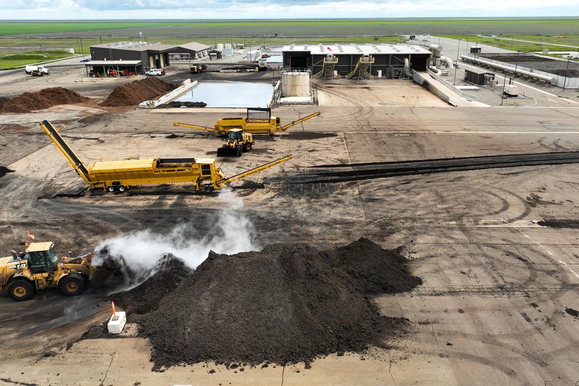 Heavy machinery and piles of compost at a sprawling facility.