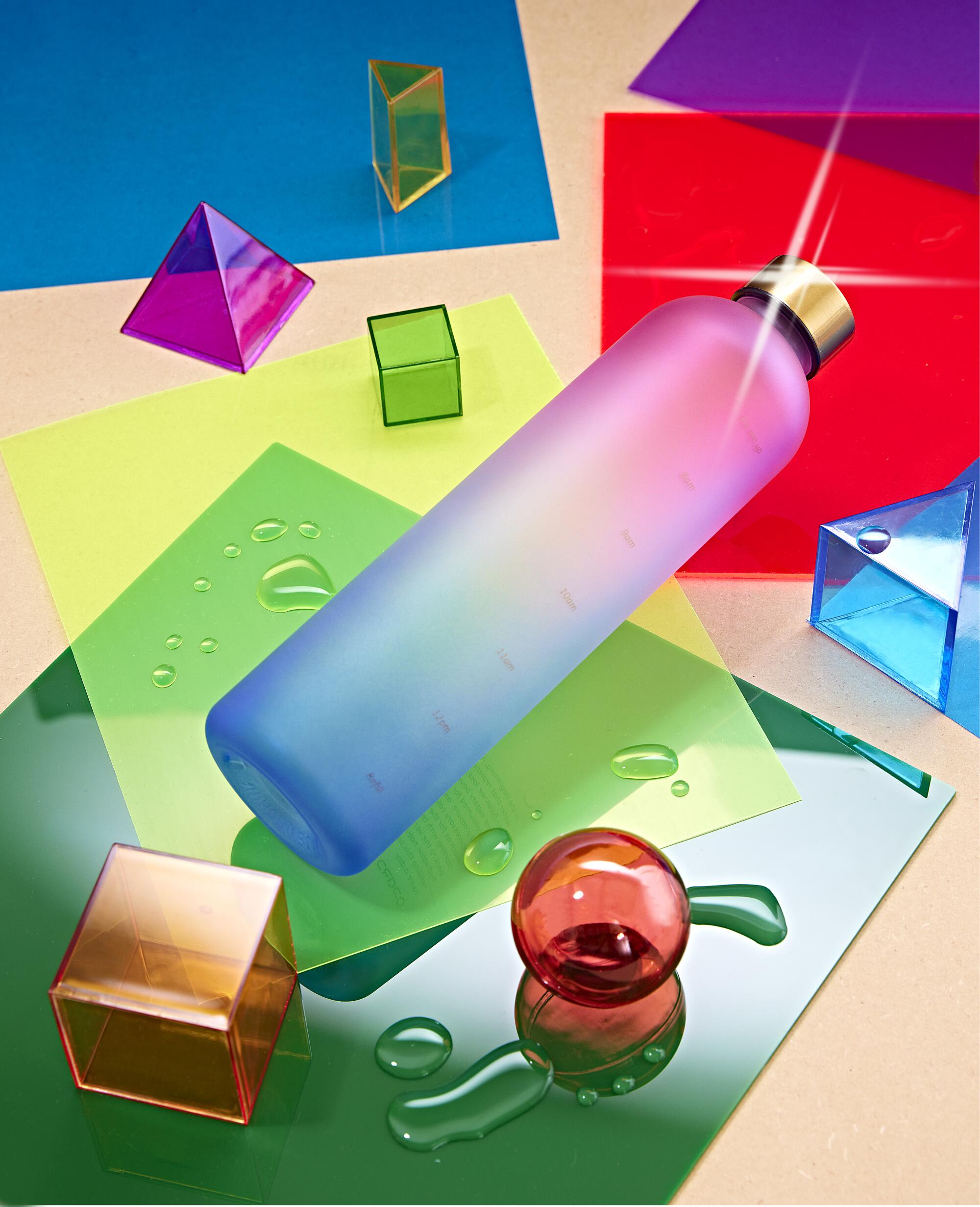 Still-life image of an eco-friendly water bottle surrounded by colorful paper and geometric objects.
