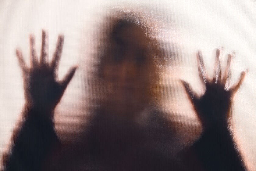 silueta de una mujer con las manos apretadas contra una ventana de cristal.  
