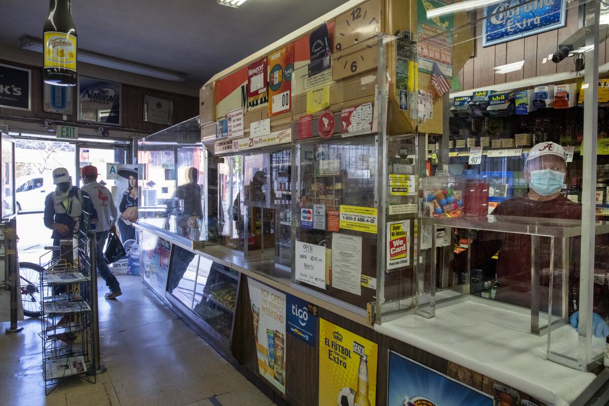 Store clerk Rutilio Lopez (CQ), right, waits for customers at the Royal Liquor Mart on Saturday, April 4, 2020 in West Adams, CA.