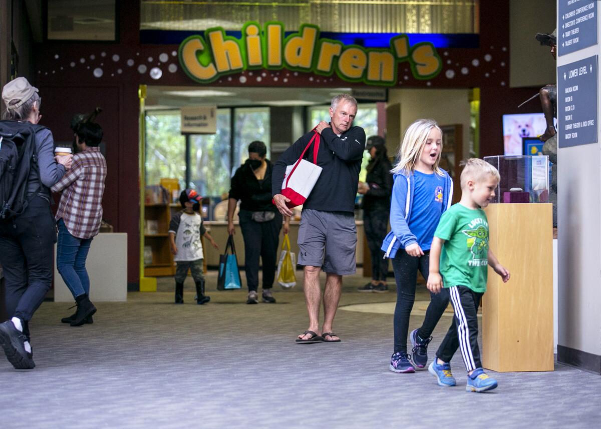 People and children walk in front of a large sign for the children's section of the Huntington Beach library