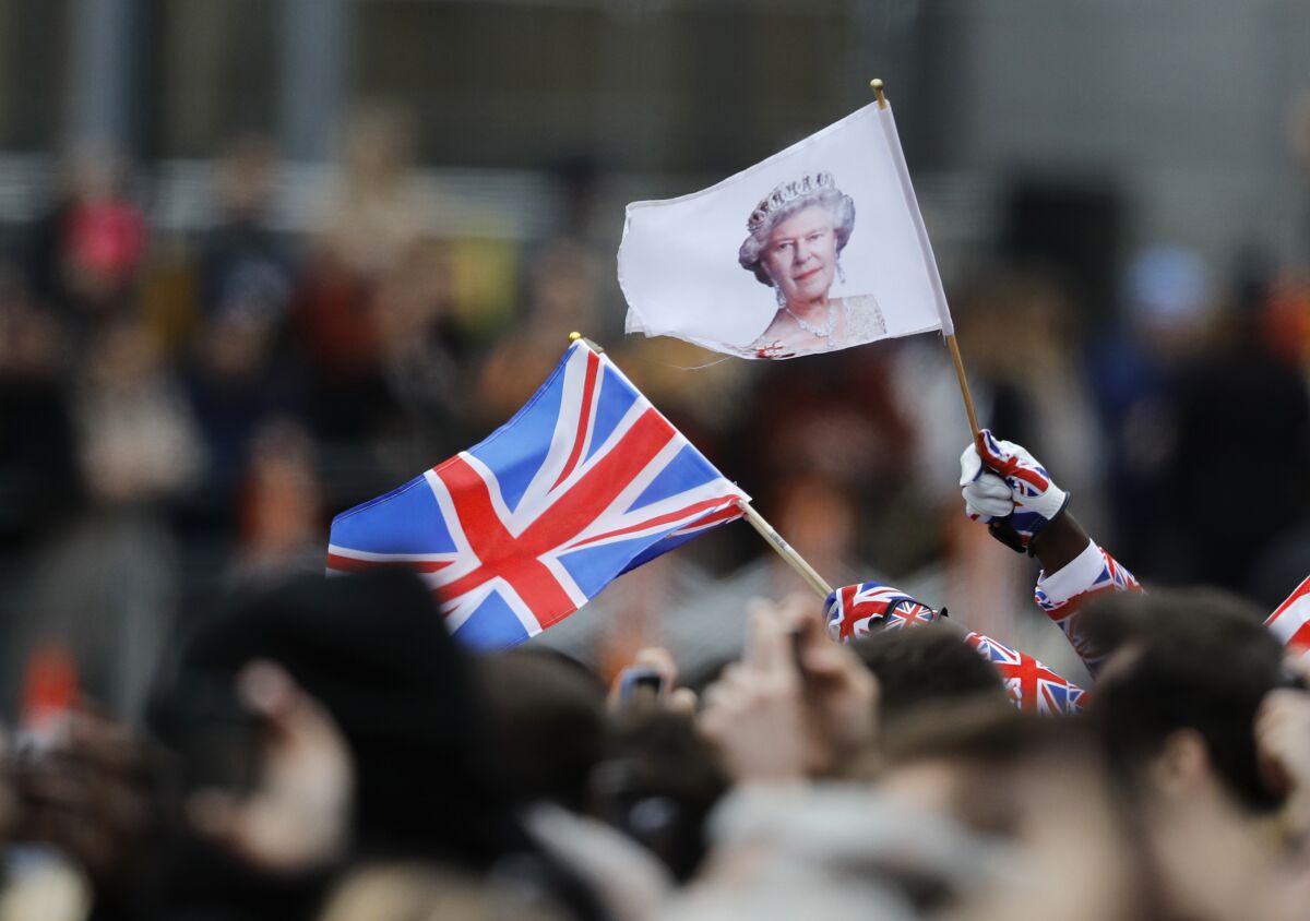 People wave the British union jack flag and a flag bearing the image of Britain's Queen Elizabeth II.