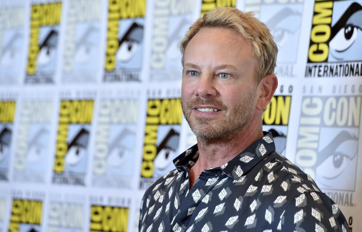 Ian Ziering poses in a patterned shirt against a Comic-Con backdrop