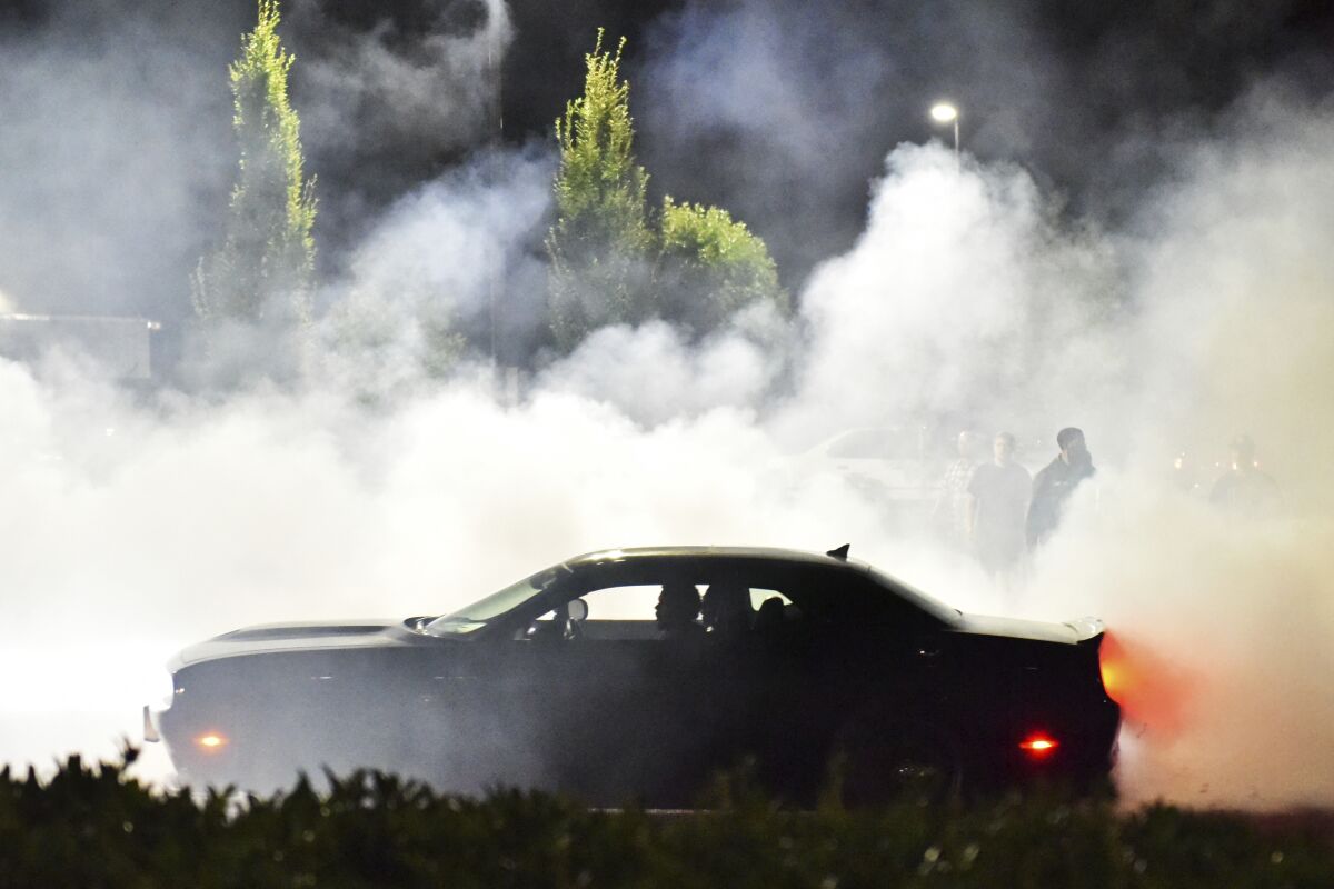 Street racers gather the evening of Sunday, Aug. 12, 2018, in the parking lot of the Goodwill on Northeast Marine Drive and 122nd Avenue in Portland, Ore. Across America, police are confronting illegal drag racing whose popularity has surged since the coronavirus pandemic and lockdowns began. Drivers have blocked off roads to race and to etch donut patterns on pavement with the tires of their souped-up cars. From Portland, Oregon; to Albuquerque, New Mexico; from Nashville, Tennessee; to New York City, officials are reporting a dangerous, and sometimes deadly, uptick in street racing.(Anna Spoerre /The Oregonian via AP)