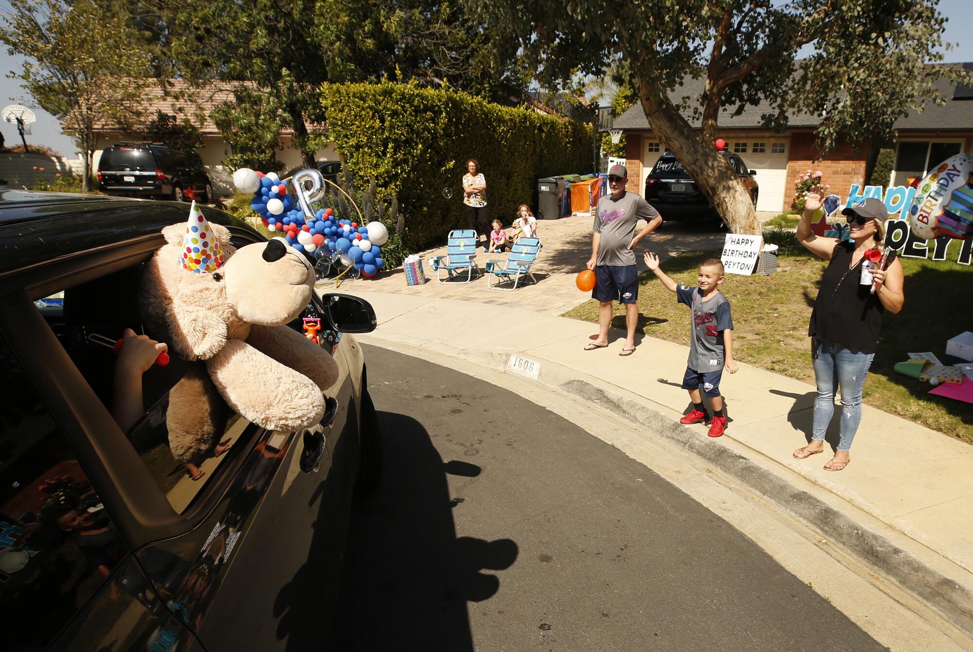 A waving Peyton is accompanied by his parents Jill and Daniel Buss as teammates drive by their home.