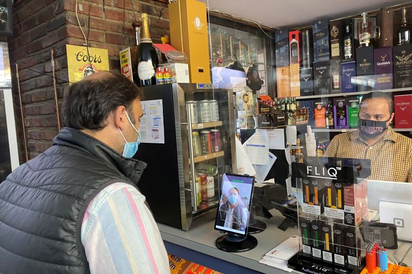 "Sid Dilawri (left), owner of Modern Liquors store in Washington DC, uses RealNetworks' MaskCheck app to see if his mask is worn properly while a store clerk looks on."