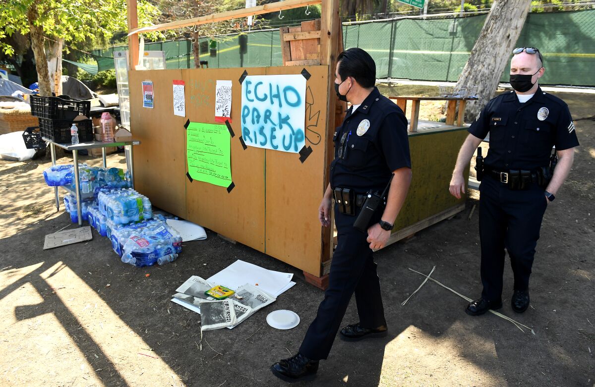 Two police officers look over water bottle cases and other belongings left behind.