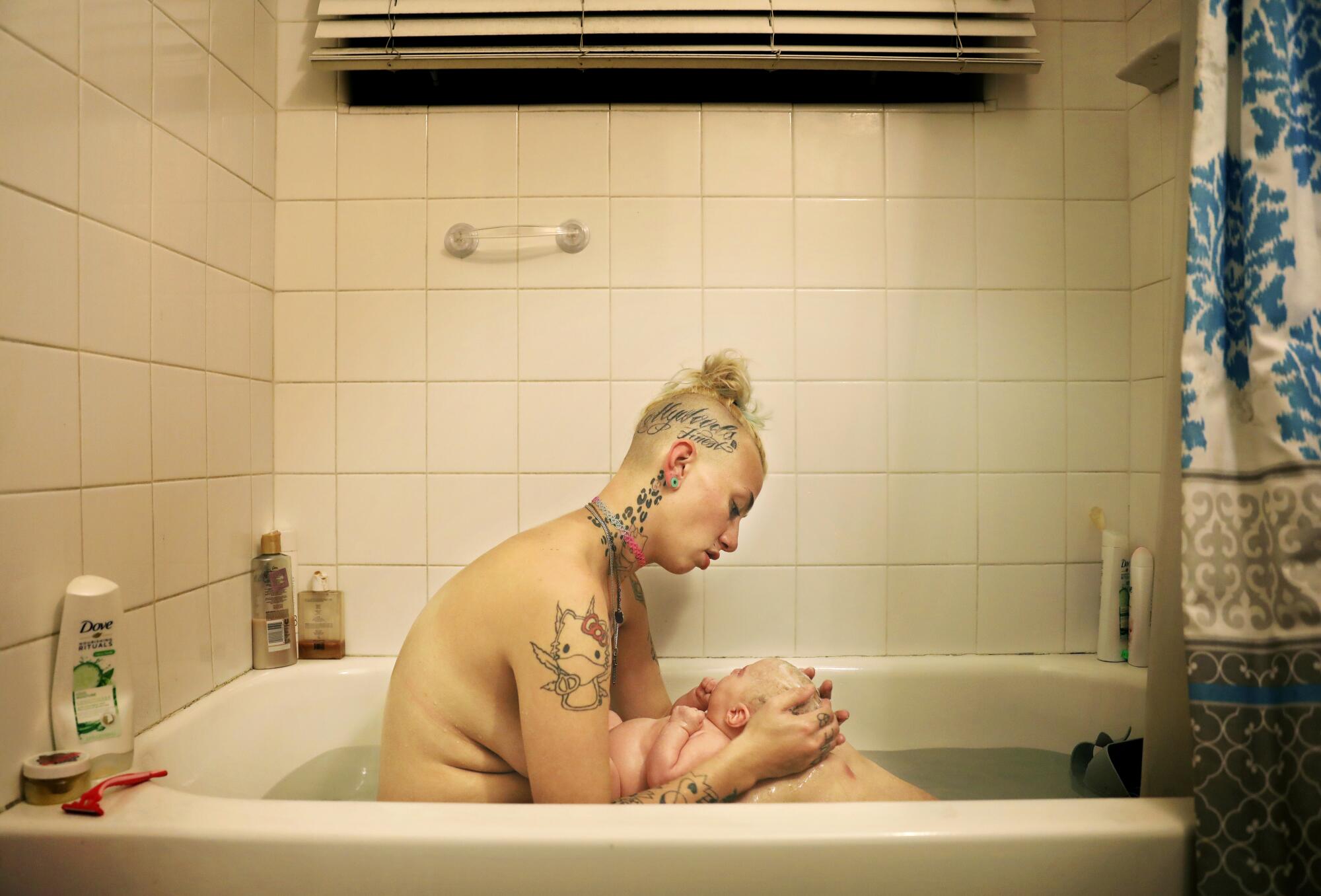 A woman naked in a bathtub holding a baby in her lap.