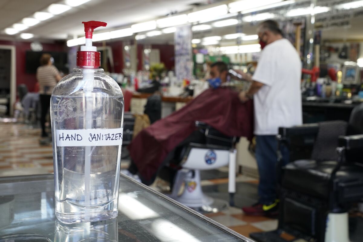 A bottle of hand sanitizer sits on a counter as Edgar Gomez has his hair cut by George Garcia, owner of George's Barber Shop, Tuesday, July 14, 2020, in San Pedro, Calif. Gov. Gavin Newsom this week ordered that indoor businesses like salons, barber shops, restaurants, movie theaters, museums and others close due to the spread of COVID-19. (AP Photo/Ashley Landis)