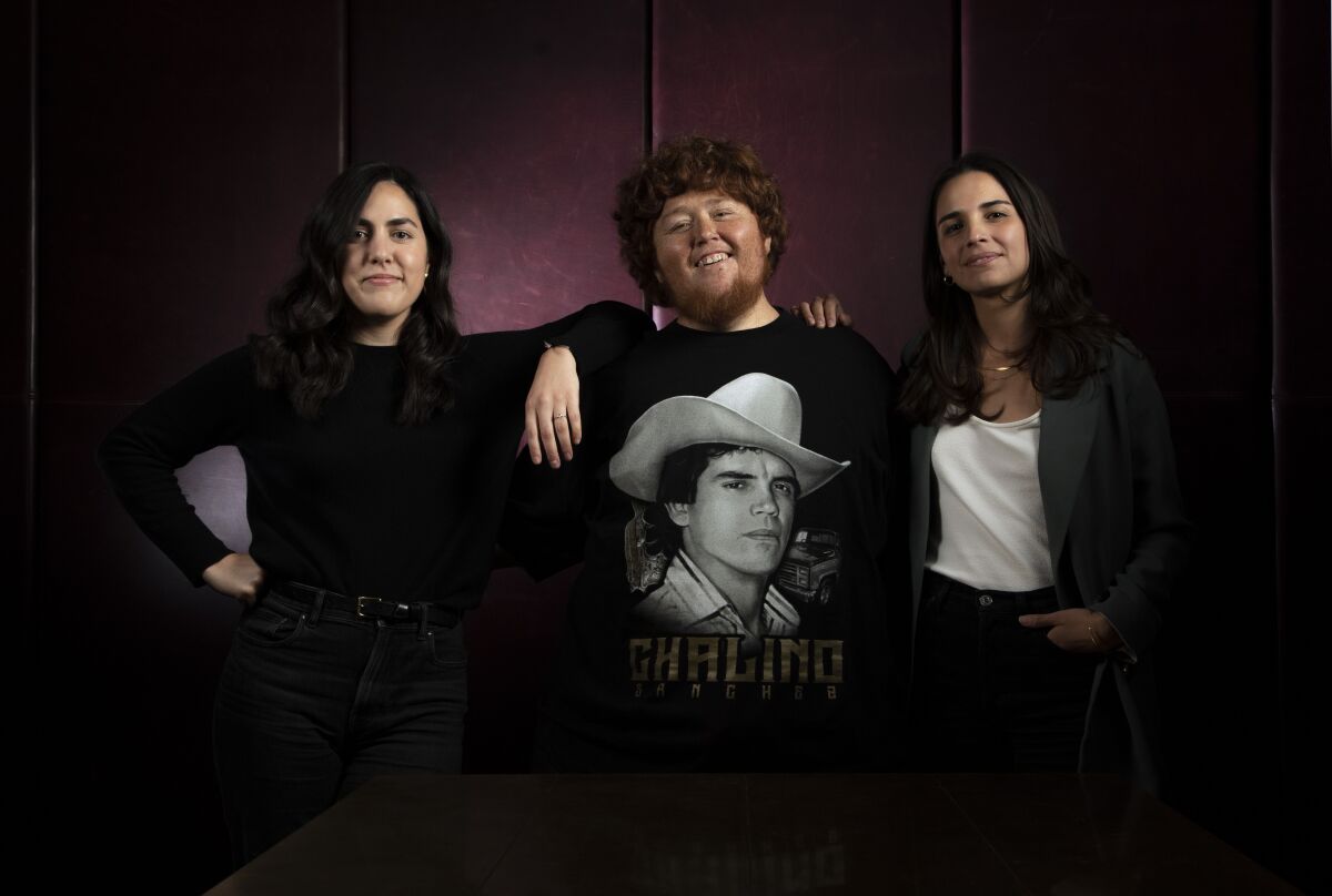 Three people, the middle one wearing a "Chalino Sánchez" T-shirt. 