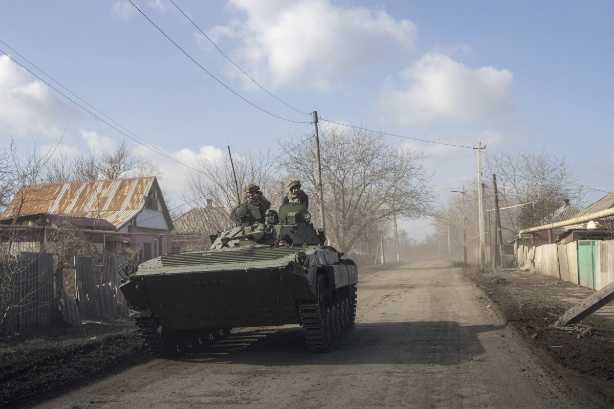 Ukrainian troops in a military vehicle drive down a road past buildings.