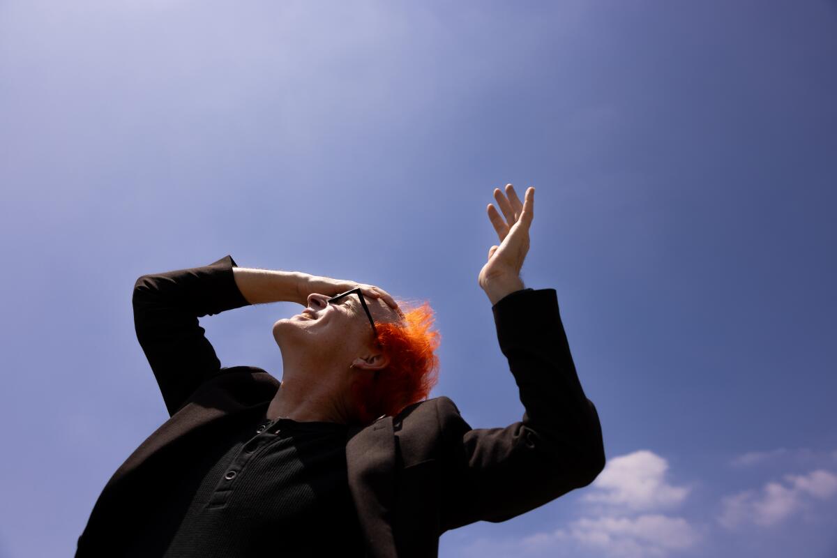 Man with orange hair looks up at sky with hand on his head