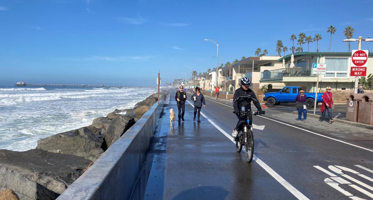 People walk on the ocean-soaked Strand in Oceanside late Friday morning.