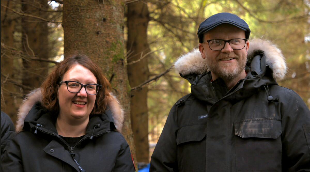 Sarah and Barrie Gower outside amid big trees and wearing heavy coats.
