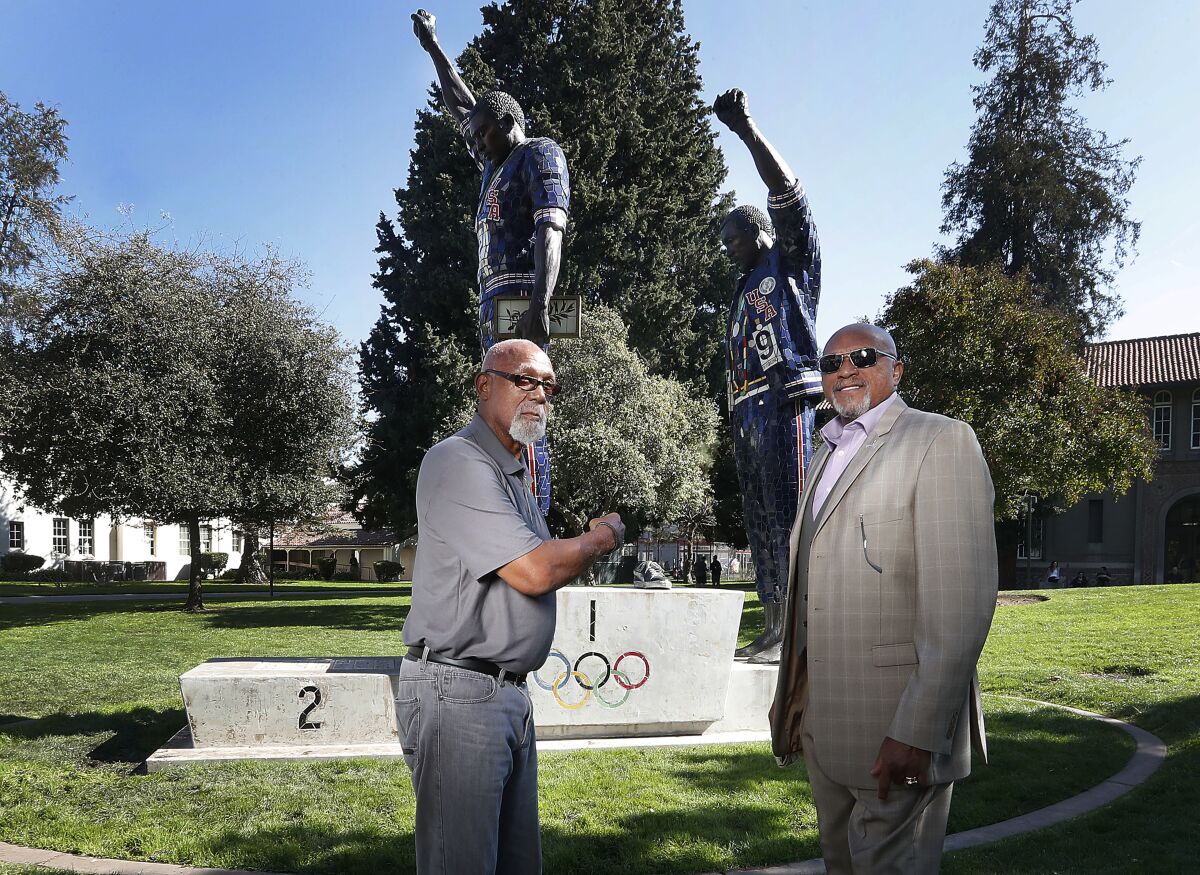 John Carlos and Tommie Smith pose for a photo in front of statue that honors their iconic protest at the 1968 Olympic Games.