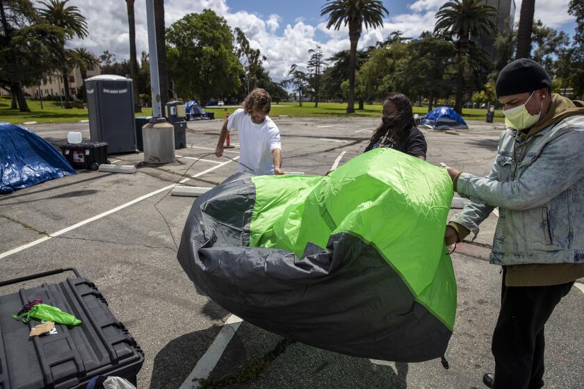 LOS ANGELES, CA - APRIL 08: VA community outreach worker Michelle O'Neal, center, helps homeless veterans Larry McNearney, 47, left, and Timothy Cornejo, 31, right, set up Cornejo's tent in a VA parking lot on Wednesday, April 8, 2020 in Los Angeles, CA. The VA is providing meal, tents, restroom facilities and security at the site. (Brian van der Brug / Los Angeles Times)