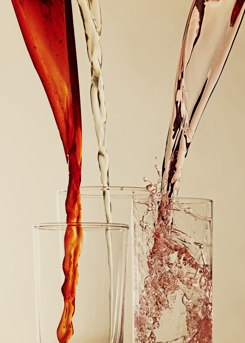 Three different colored beverages are poured into separate glasses.