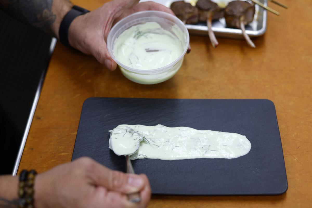 A chef lays down tzatziki sauce on a board before adding the lamb atop it.