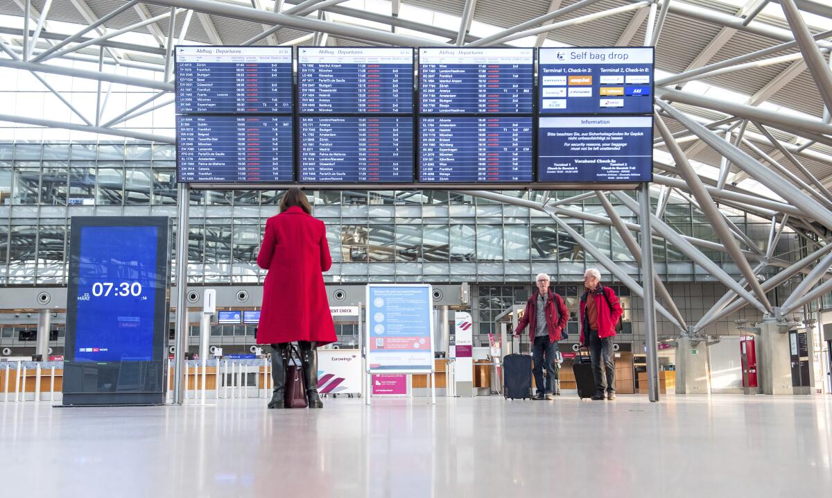 Travelers stand in front of a display board in an airport terminal in Hamburg, Germany, in the morning of Tuesday, March 22, 2022. Due to a warning strike by the trade union ver.di, the security checkpoint remains closed all day and no departures take place. (Daniel Bockwoldt/dpa via AP)