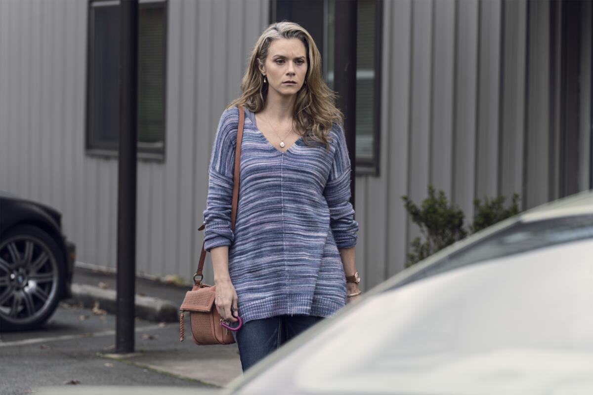 Hilarie Burton Morgan as Lucille walks while carrying a purse with a long strap