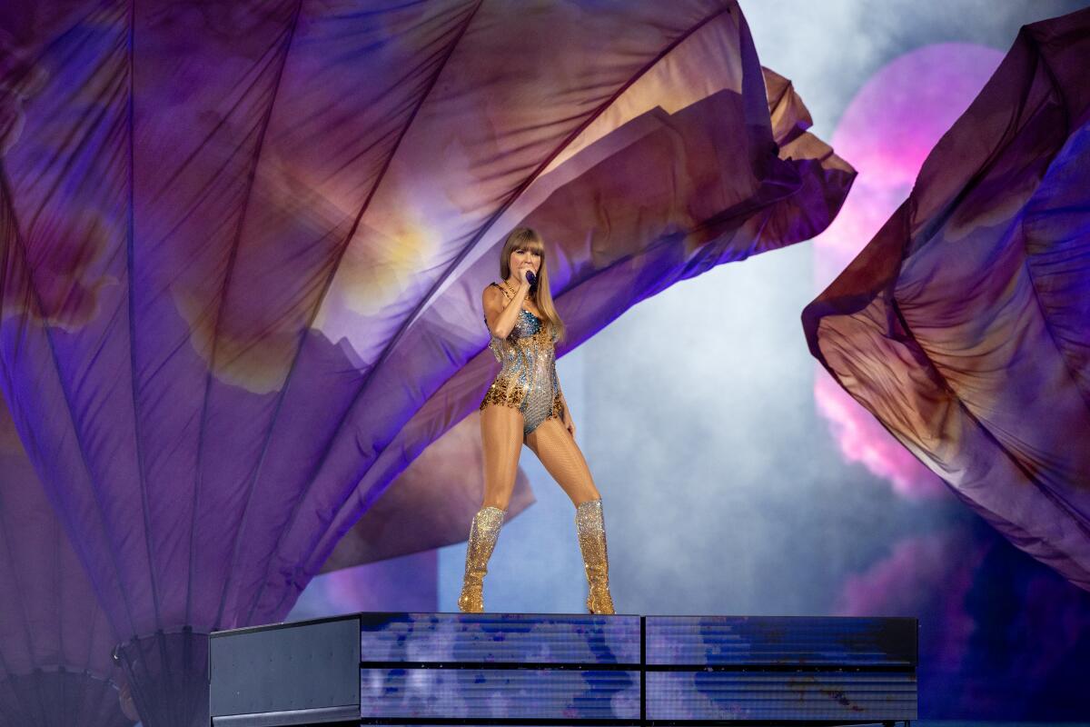 Taylor Swift wears a silver, orange and blue leotard with silver and orange boots as she sings onstage