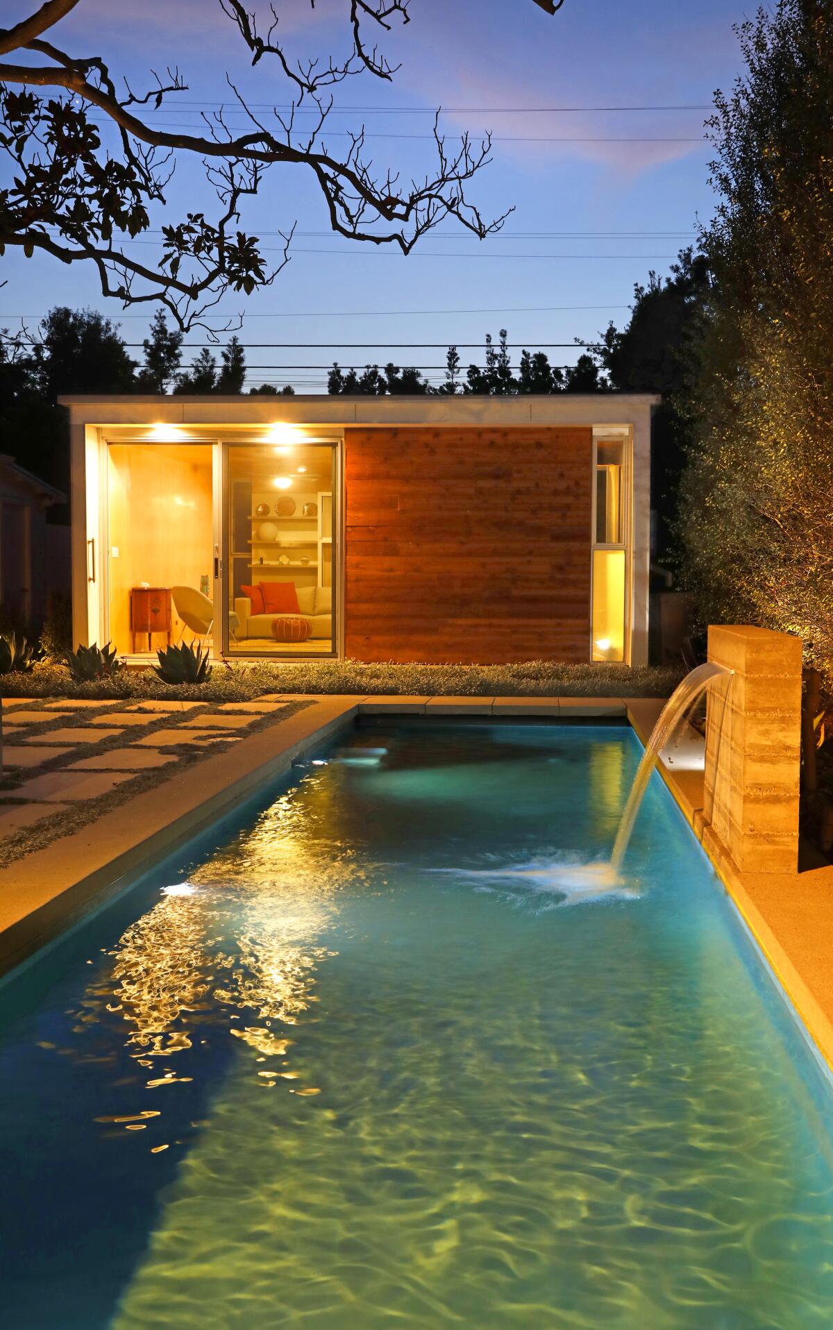 An ADU sits beyond a lap pool with a waterfall feature.