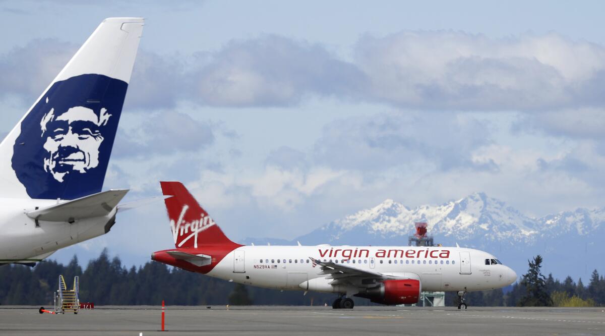 A Virgin America plane taxis past an Alaska Airlines plane waiting at a gate at Seattle-Tacoma International Airport. The FAA has allowed Alaska Airlines and Virgin America to consolidate under the same operating certificate.