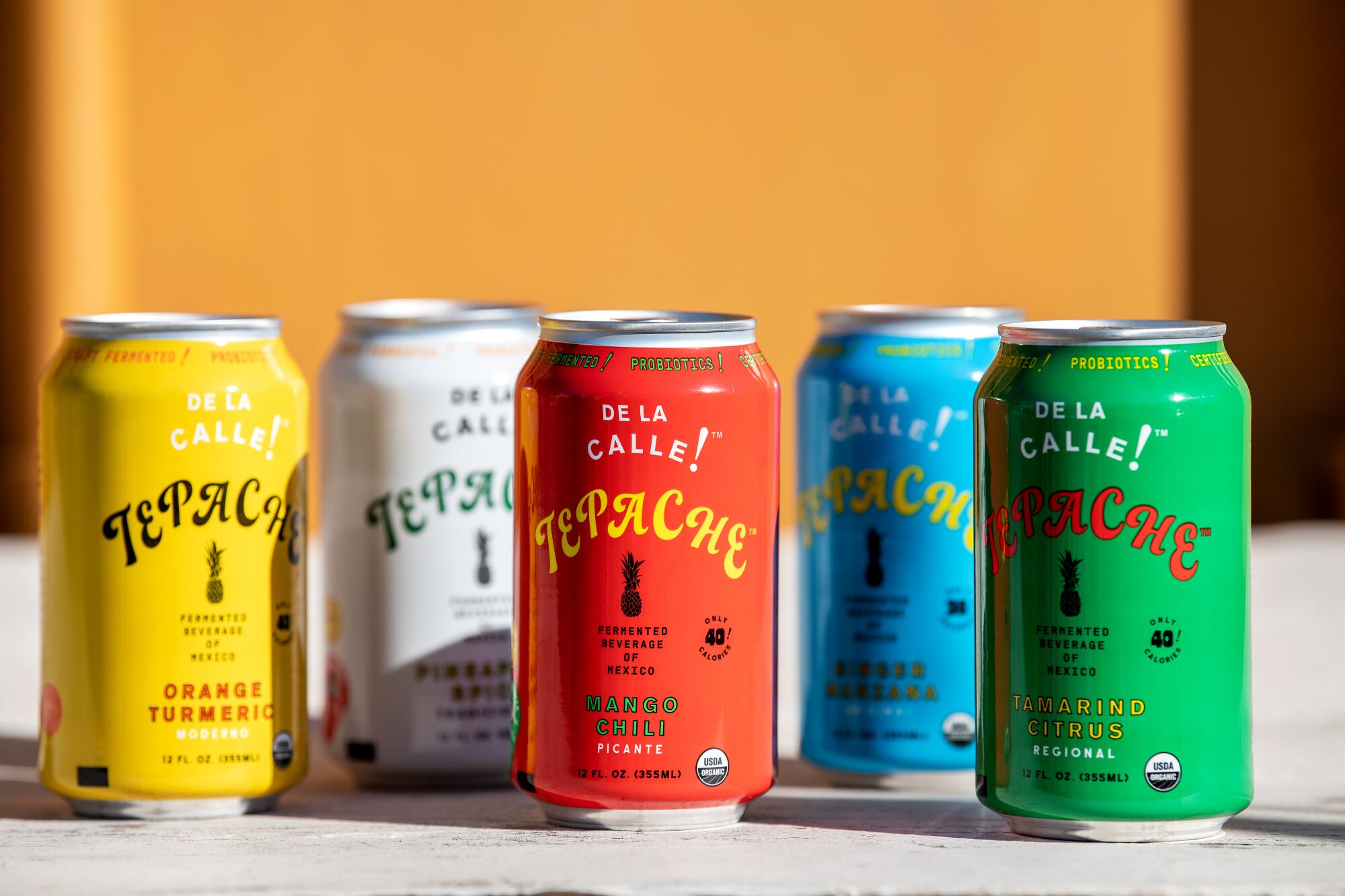 Five colorful cans of De La Calle tepache.