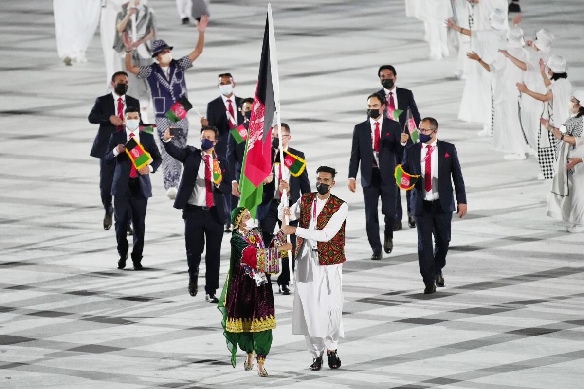 FILE - Kimia Yousofi, front left, and Farzad Mansouri, of Afghanistan, carry their country's flag during the opening ceremony in the Olympic Stadium at the 2020 Summer Olympics on July 23, 2021, in Tokyo, Japan. Afghanistan's flag bearer at the Tokyo 2020 Games and other prominent women's sports campaigners have been safely relocated to Australia following a year-long Australian Olympic Committee (AOC) project. (AP Photo/David J. Phillip, File)