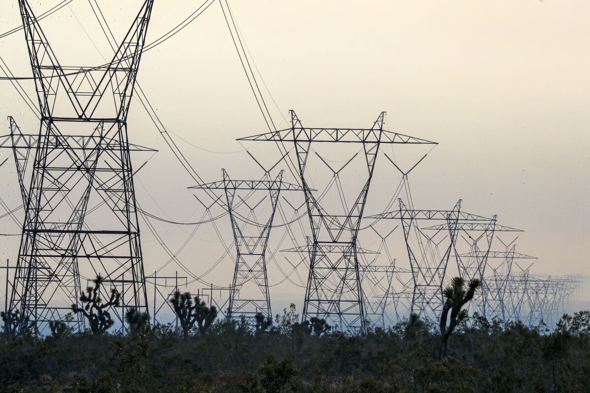 Transmission towers are seen in silhouette of a gray sky.