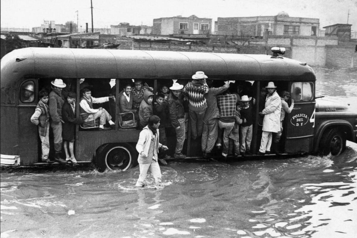 Archival photograph of people holding onto a bus or walking through flooded streets of Mexico City. 