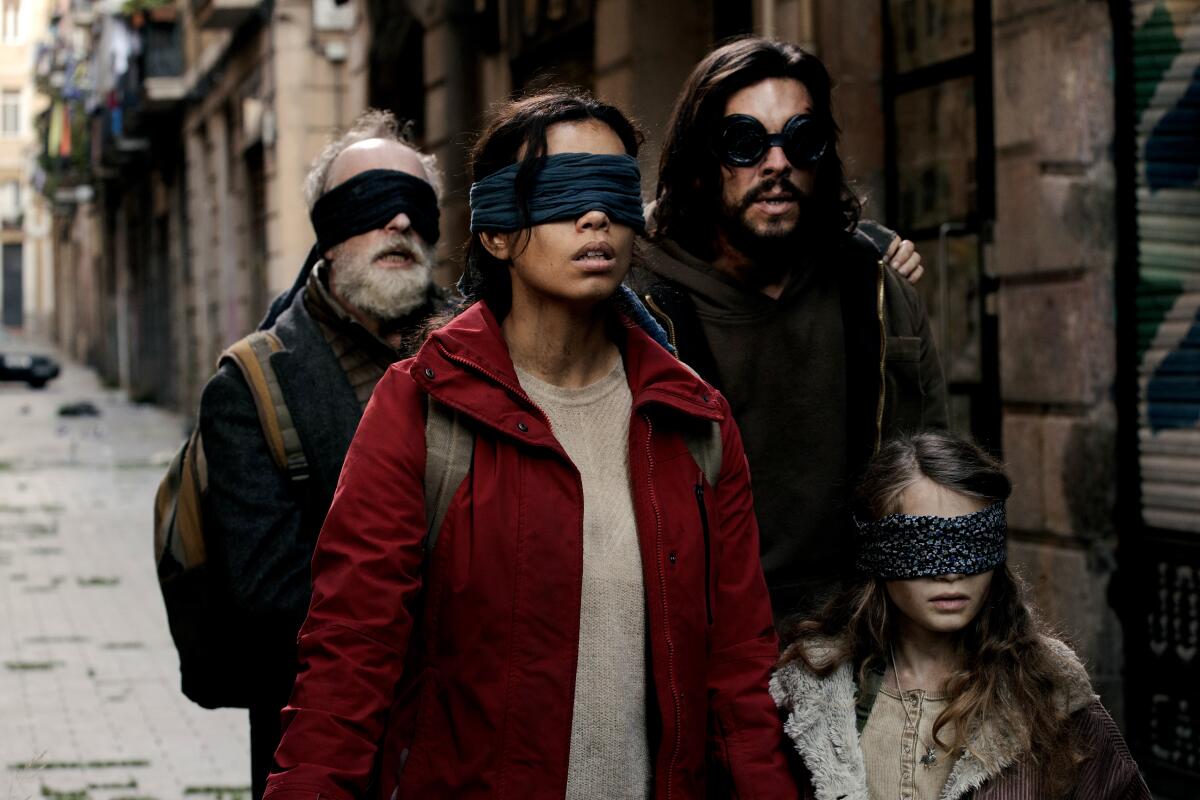 Four people in blindfolds make their way down a Spanish street