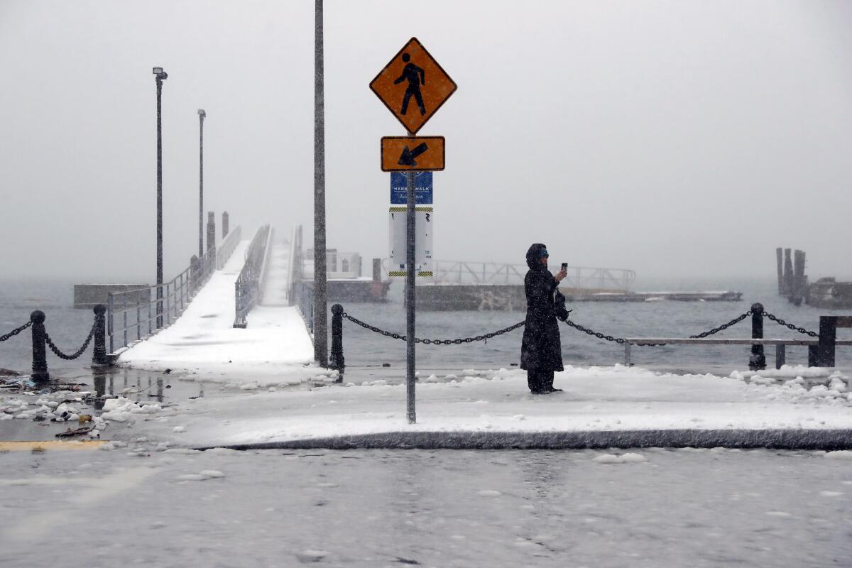A person stands between a snowy harbor and a flooded roadway during a storm