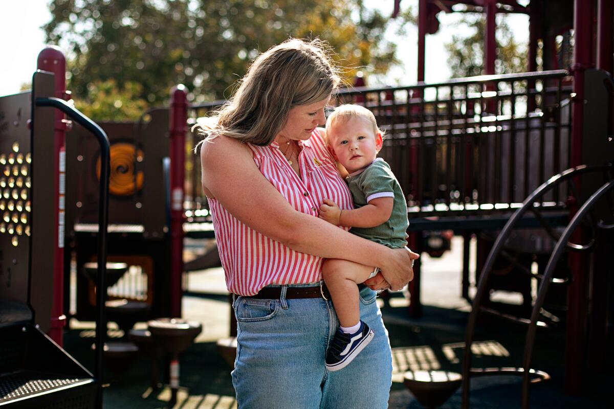 A woman holds a toddler in a playground