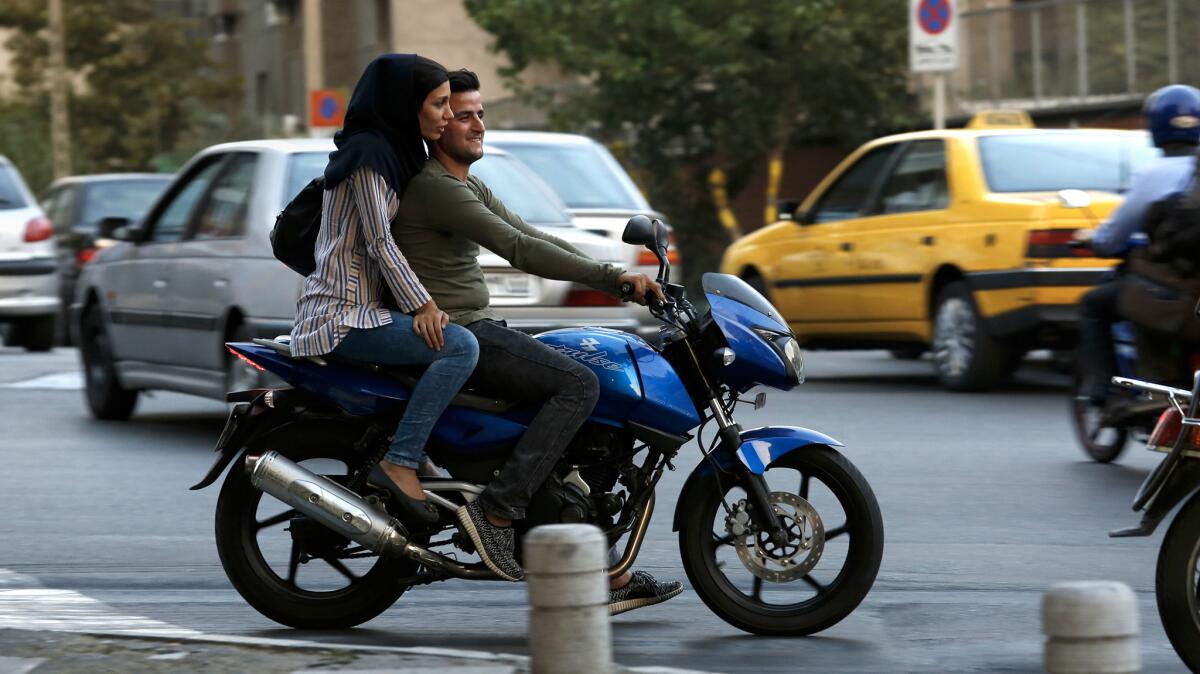 A woman rides on the back of a motorcycle in Tehran.