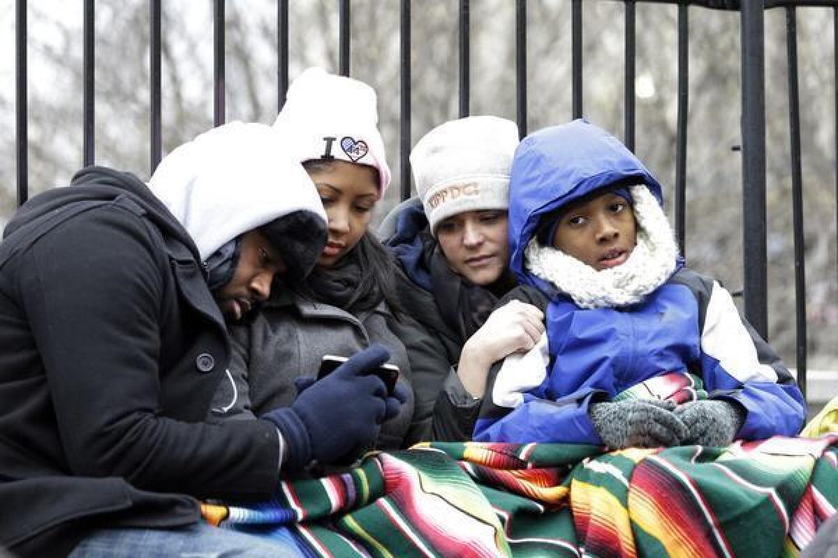 Bundled up against the chill, Augustus Jones, left, Joi Baker, Kristen Conliss and Makhi Inge watch the inaugural ceremonies on a smartphone Monday in Washington.