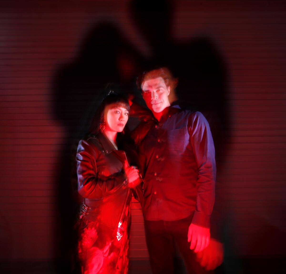Actors Constance Wu and Finn Wittrock pose in a dim setting, bathed in spooky red light.
