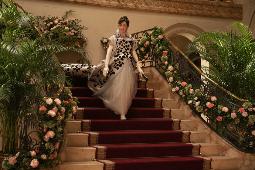A woman in a long gown walks down a flight of stairs lined with flowers.
