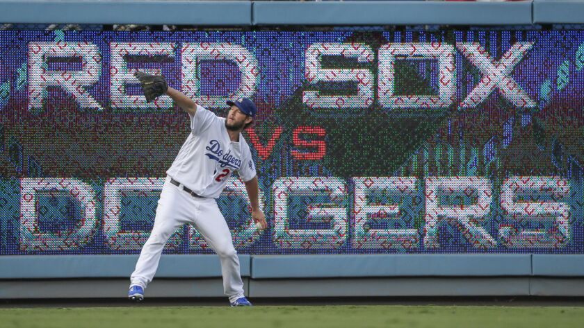 Clayton Kershaw holds up his glove in front of a Red Sox vs. Dodgers sign.